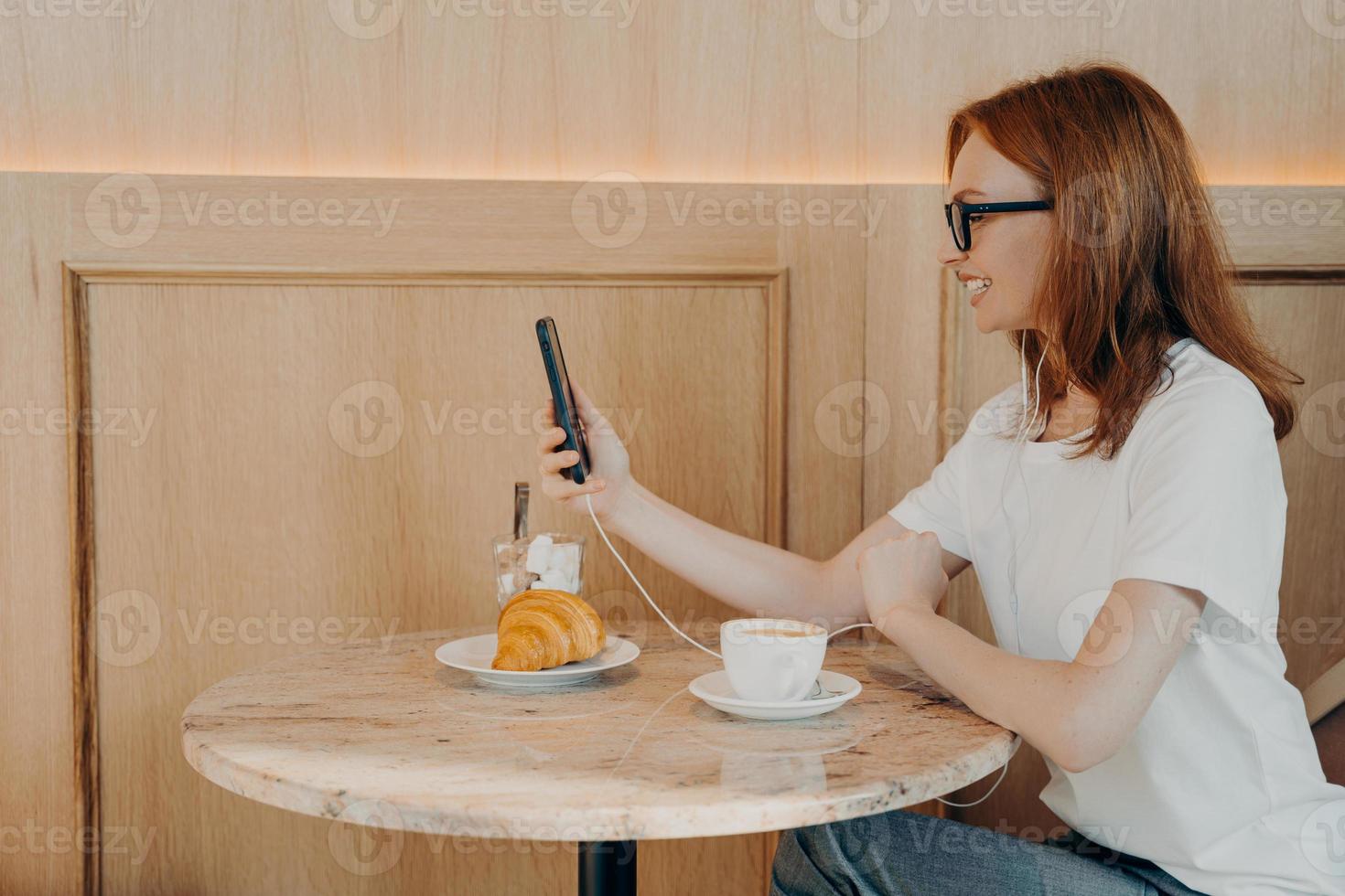 Une jeune femme rousse heureuse utilise une connexion en itinérance est assise à table dans un café photo