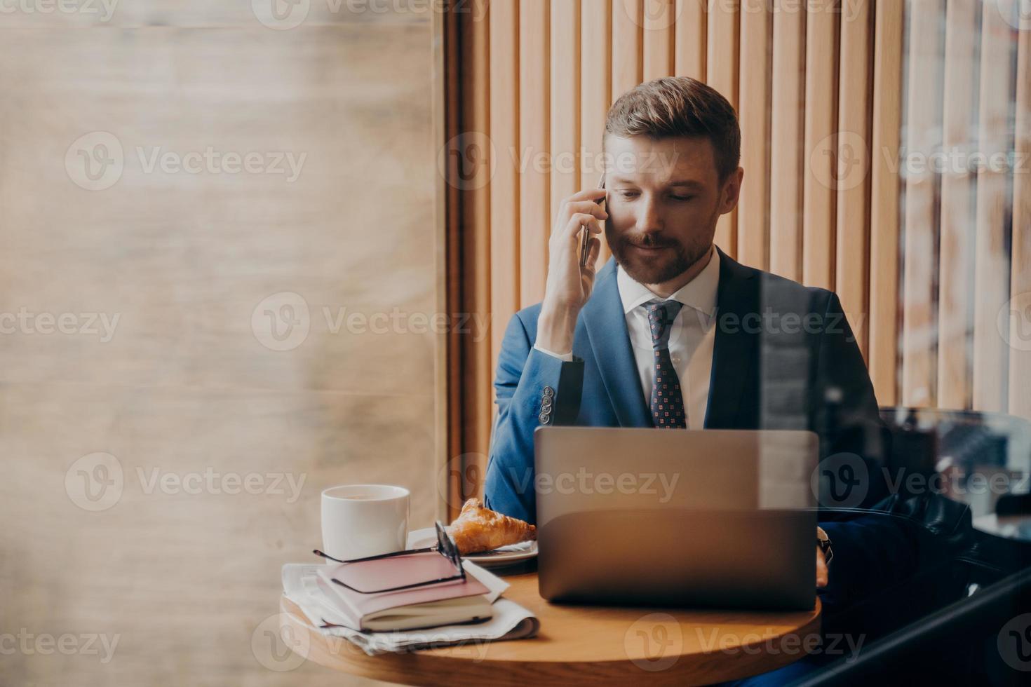 portrait d'un homme des finances élégant en costume élégant assis dans un café avec un ordinateur portable ouvert photo