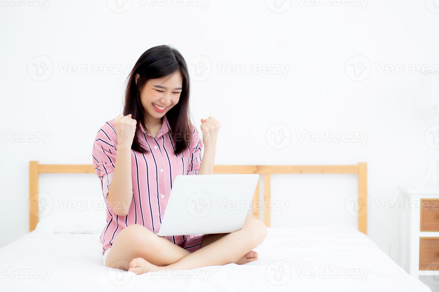 belle de portrait asiatique jeune femme assise détente et loisirs avec ordinateur portable internet en ligne en vacances dans la chambre, gaie d'asie fille avec geste heureux et succès, concept de style de vie. photo