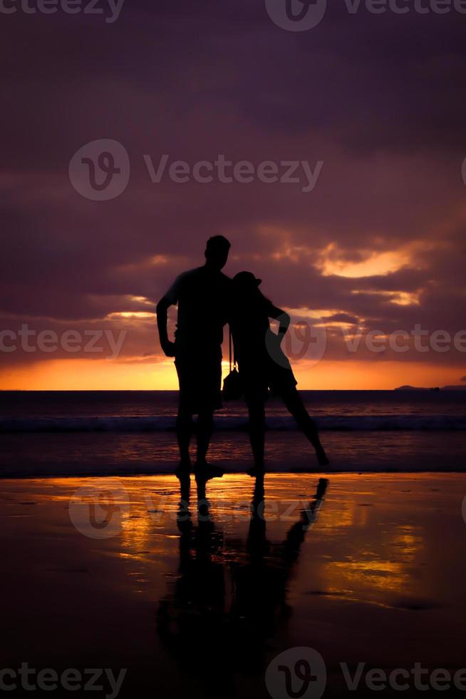 silhouette de couple se tiennent la main et heureux jeune couple aime sur la plage au coucher du soleil photo