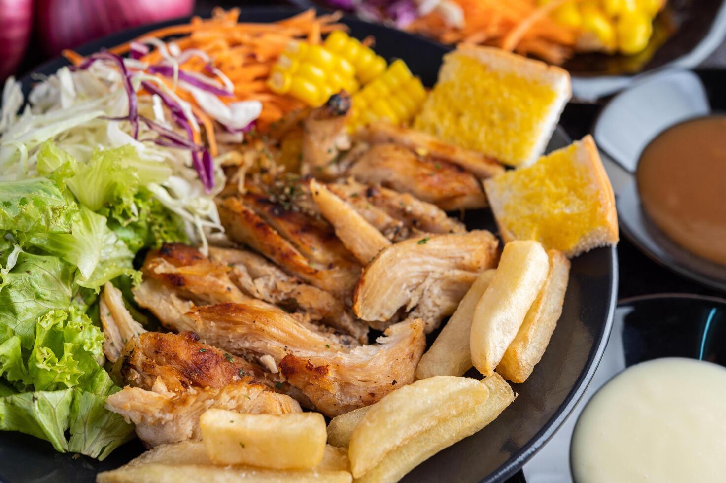 steak de poulet avec pain, carottes, chou-fleur, navets et maïs sur une assiette noire. photo