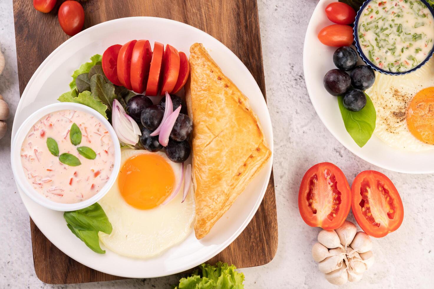 le petit-déjeuner se compose de pain, œuf au plat, vinaigrette, raisins noirs, tomates. photo