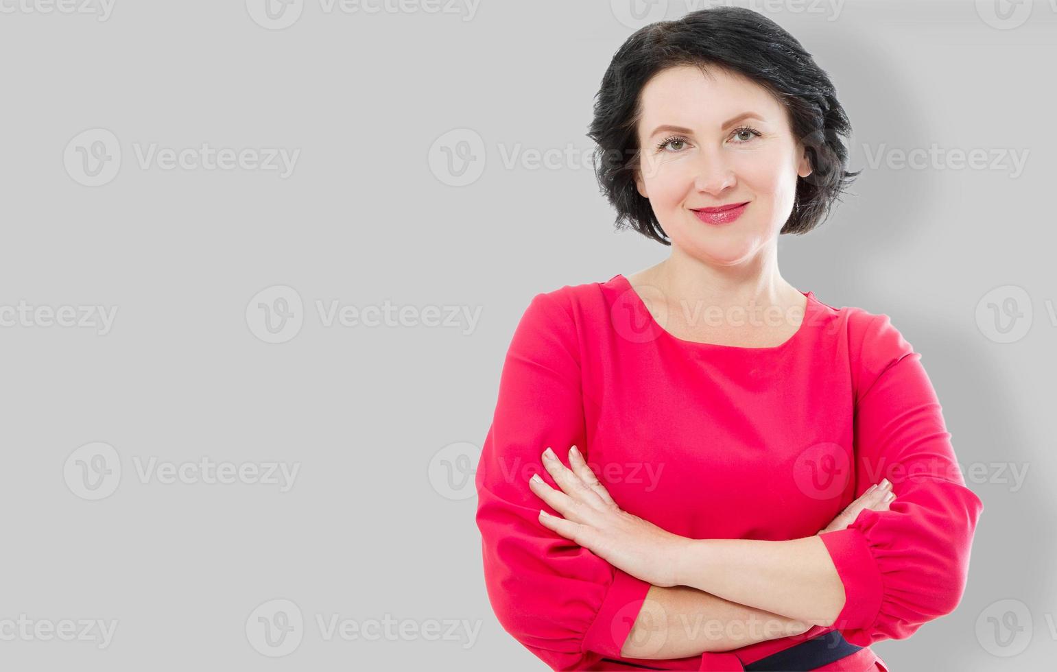 femme souriante d'âge moyen en robe rouge et bras croisés isolés sur fond gris. concept de maquillage et de beauté. copie espace photo