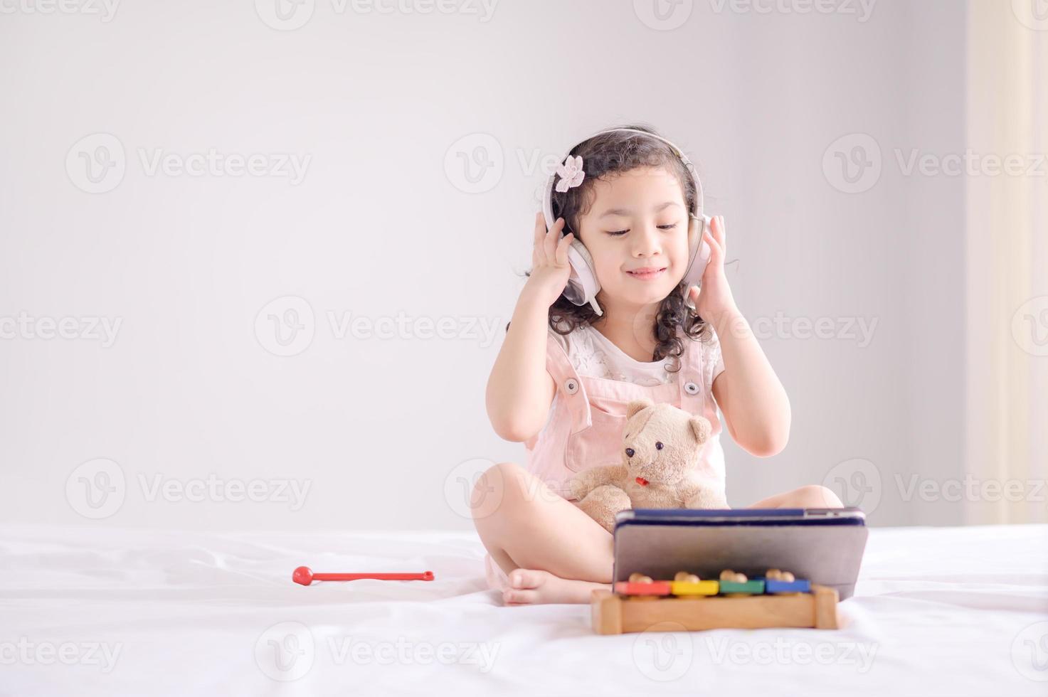 une jolie fille asiatique utilise joyeusement une tablette pour écouter de la musique et apprendre dans la chambre photo