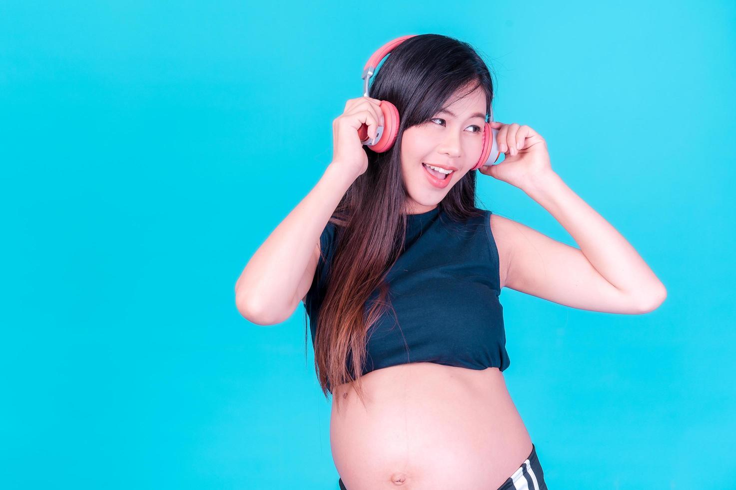 belle femme enceinte asiatique se tient détendue et aime écouter de la musique sur des écouteurs connectés à internet photo