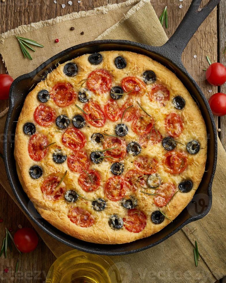 focaccia, pizza à la poêle, pain plat italien aux tomates, olives et romarin. table en bois photo