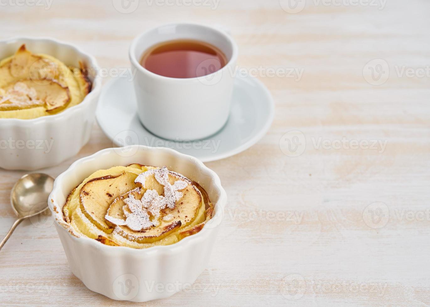 gâteau aux pommes et tasse de thé sur une table en bois blanc dans la cuisine. dessert au caillé délicat avec pommes, flocons d'amandes et cannelle, vue latérale photo