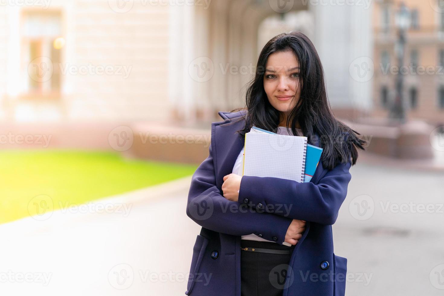 belle fille souriante étudiante brune tenant des cahiers et des manuels, se tient à l'université dans la rue de st. petersbourg. une charmante femme aux longs cheveux noirs étudie au cours photo