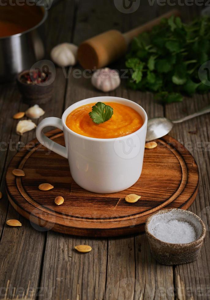 soupe à la crème de pupmkin dans une tasse sur une table en bois marron, verticale, vue latérale. purée végétarienne diététique sur planche à découper avec persil, ail. photo