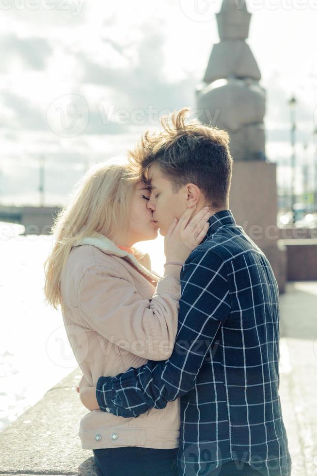 le garçon regarde tendrement la fille et veut l'embrasser. un jeune couple se tient enlacé. le concept de l'amour chez les adolescentes et du premier baiser, les sentiments sincères de l'homme et de la femme. la ville, le front de mer. vertical photo