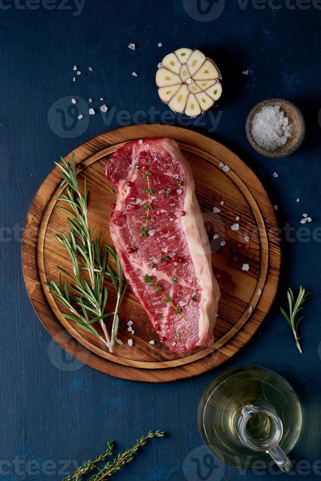 gros morceau entier de viande de boeuf crue, contre-filet sur une planche à découper en bois sur fond bleu foncé photo