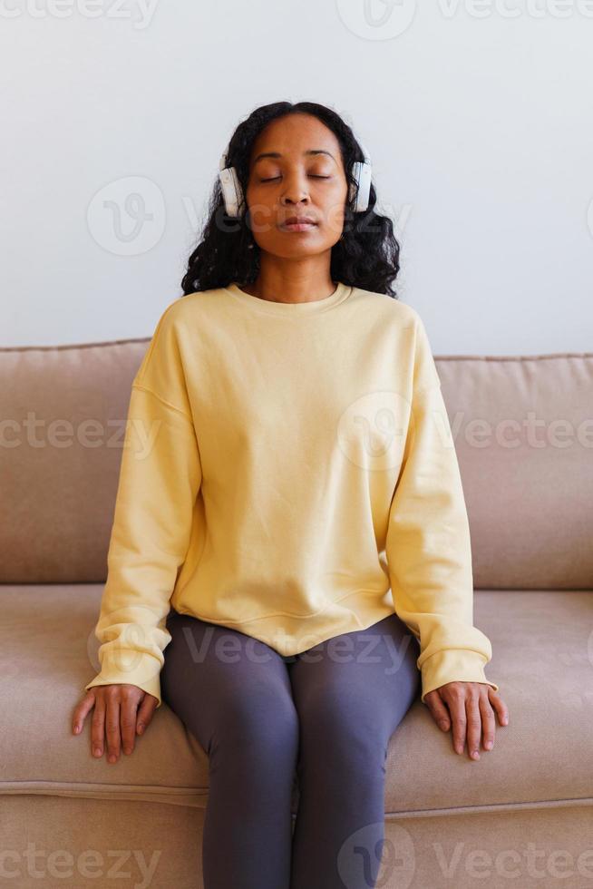 femme afro-américaine assise sur un canapé et écoutant de la musique dans des écouteurs. thérapie respiratoire photo