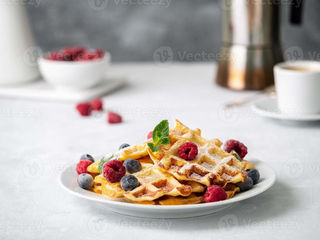 gaufres belges aux framboises, myrtilles, lait caillé et café, vue latérale. petit déjeuner maison sain, fond de béton léger photo