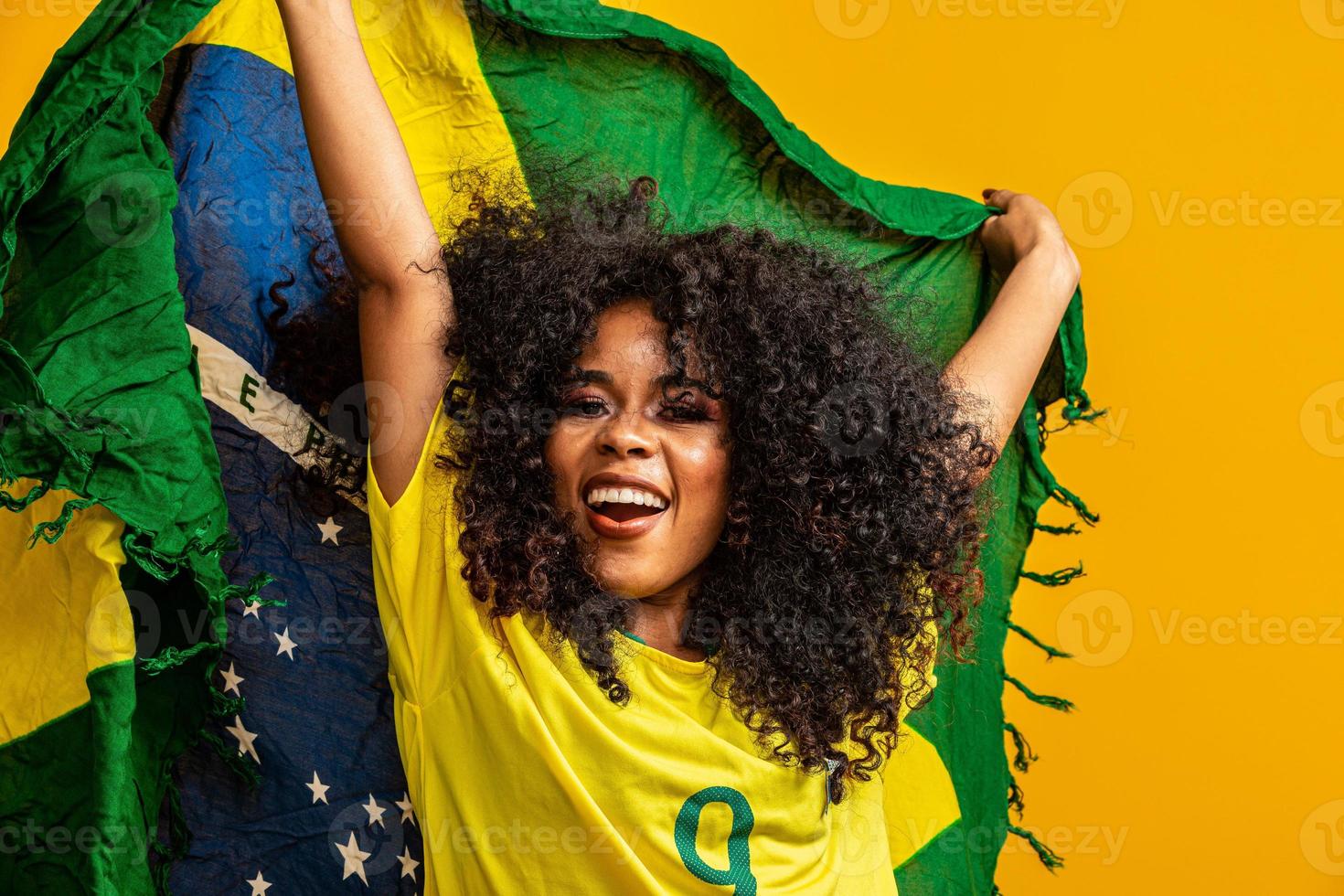 afro girl acclamant l'équipe brésilienne préférée, tenant le drapeau national sur fond jaune. photo