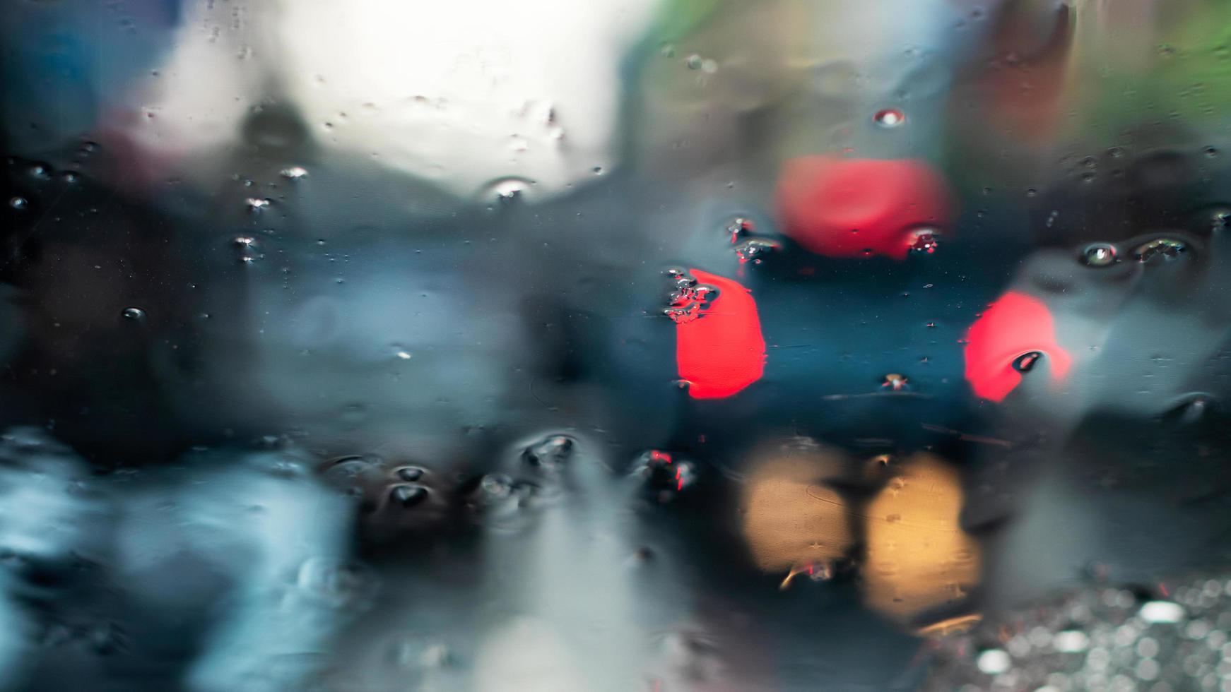 flou d'arrière-plan abstrait d'un pare-brise de voiture en regardant à travers de nombreuses gouttes de pluie jusqu'au feu rouge au bout de la voiture, qui était garée dans la rue la nuit. photo