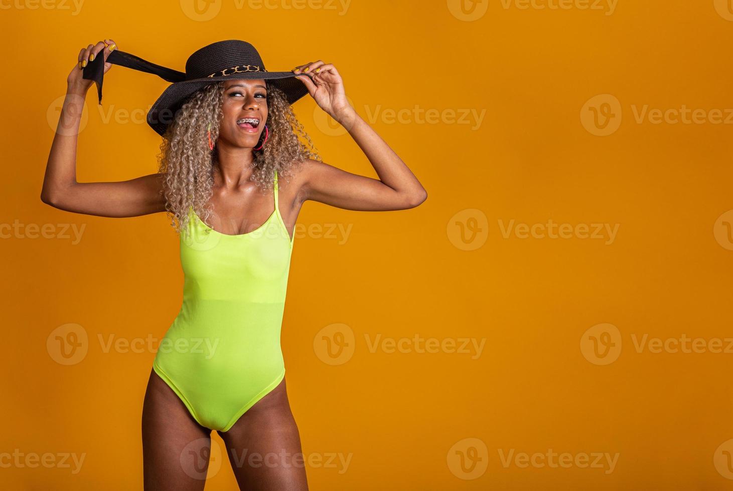 jolie fille aux cheveux bouclés dans un maillot de bain de plage vert vif, chapeau, bouche ouverte émotionnellement sur un fond jaune vif avec un corps parfait. isolée. tourné en studio. photo