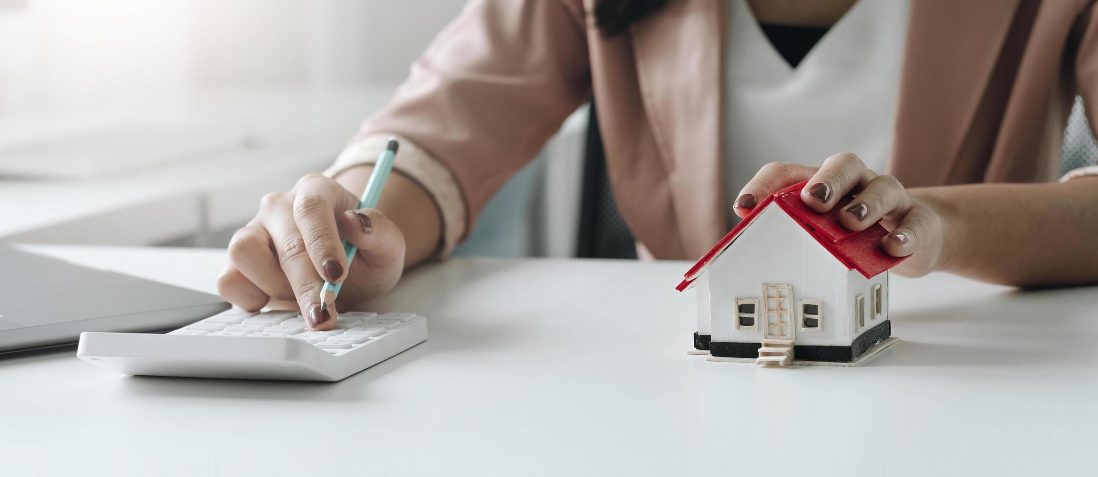 femme d'affaires avec modèle de maison faisant des finances et calculant le coût de l'investissement immobilier et dans d'autres systèmes fiscaux. concept bancaire de comptabilité de financement d'entreprise photo