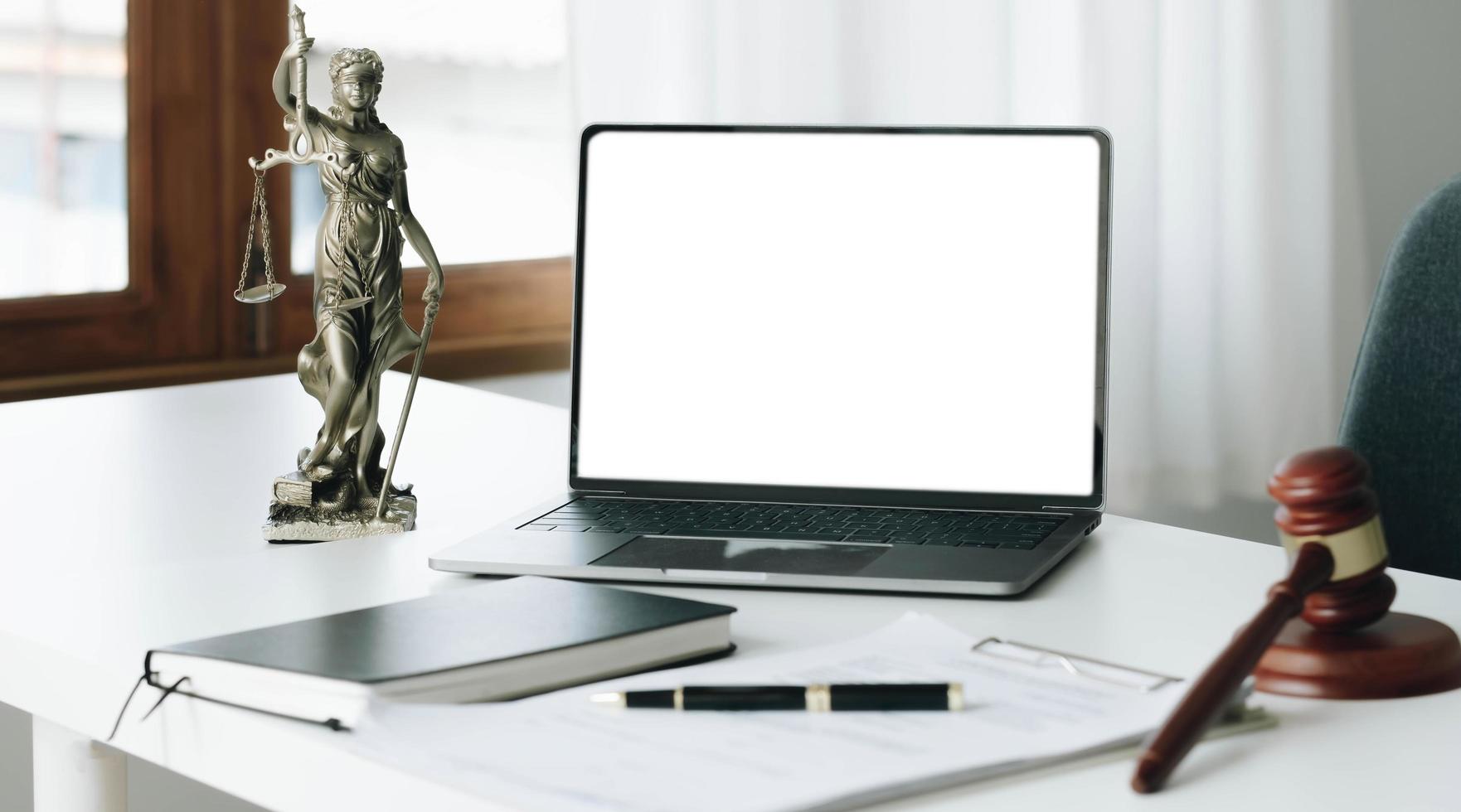 espace de travail d'avocat avec écran blanc vierge pour ordinateur portable et marteau en bois de droit, livre juridique et échelle en laiton du juge. avocat et droit, concept juridique de la salle d'audience judiciaire et législative. photo