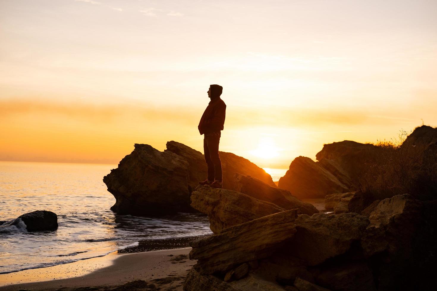 silhouette de voyageur masculin se tenir près de la falaise et regarder le beau coucher de soleil dans la mer photo