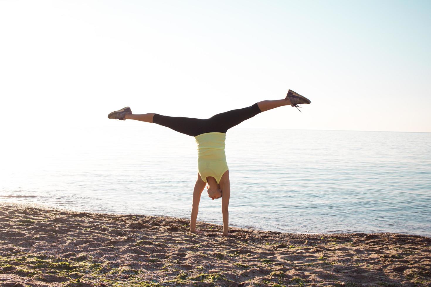 jeune femme gymnaste professionnelle danse sur la plage, exercices d'entraînement avec des junps cool, lever de soleil sur fond de mer ou d'océan photo