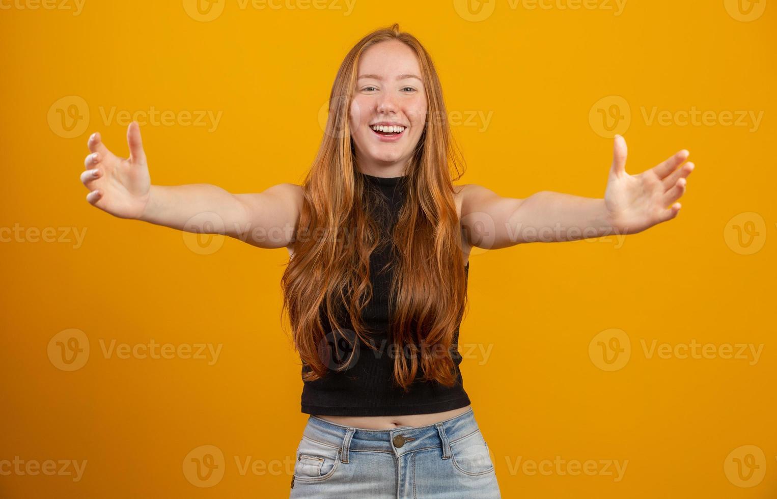 concept de vacances, de famille et de relation. tendre, magnifique femme rousse, charmante petite amie tend les bras vers quelqu'un, veut un câlin, embrasse un ami, souriant charmant et gentil, fond jaune. photo