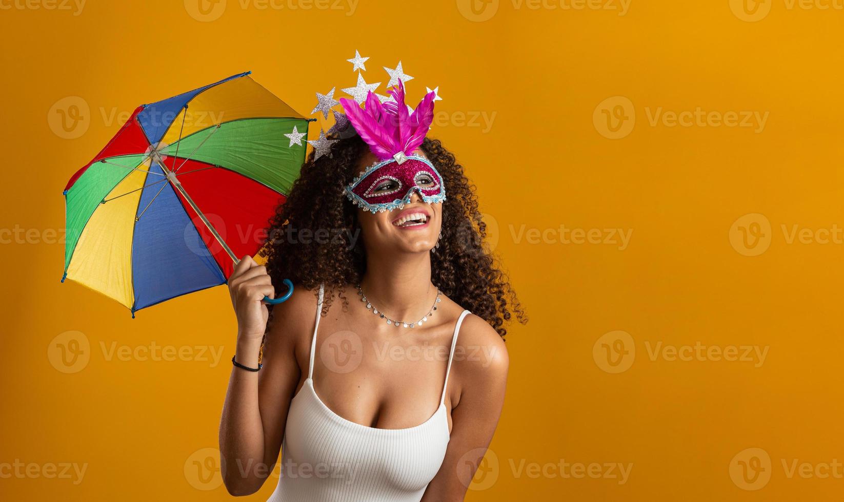 jeune femme aux cheveux bouclés célébrant la fête du carnaval brésilien avec un parapluie frevo sur jaune. photo