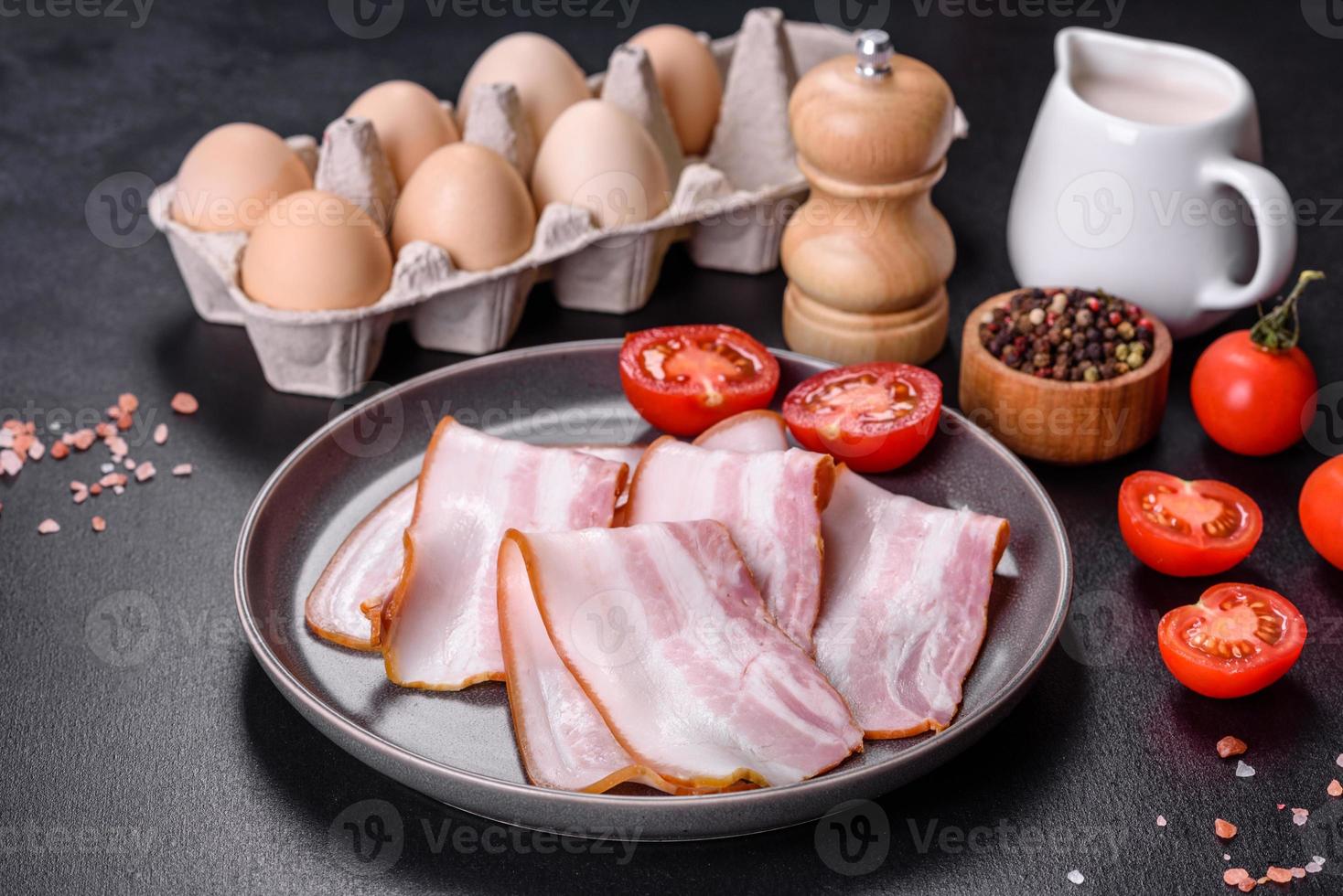 délicieux bacon cru frais coupé avec des tranches sur une plaque grise sur un fond de béton foncé photo