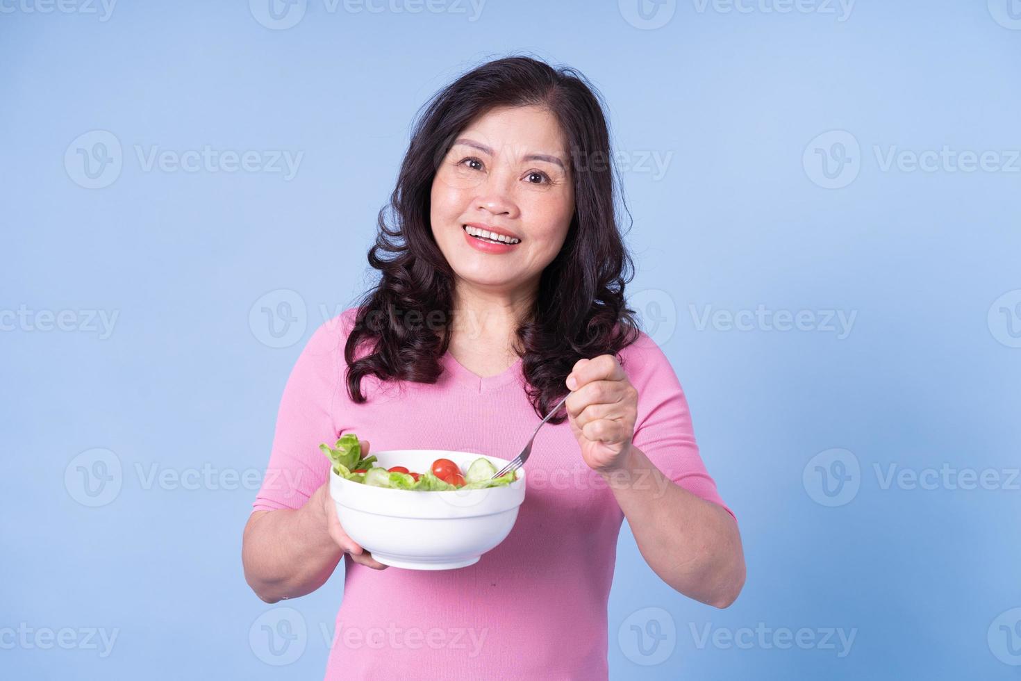 image d'une femme asiatique d'âge moyen mangeant de la salade sur fond bleu photo