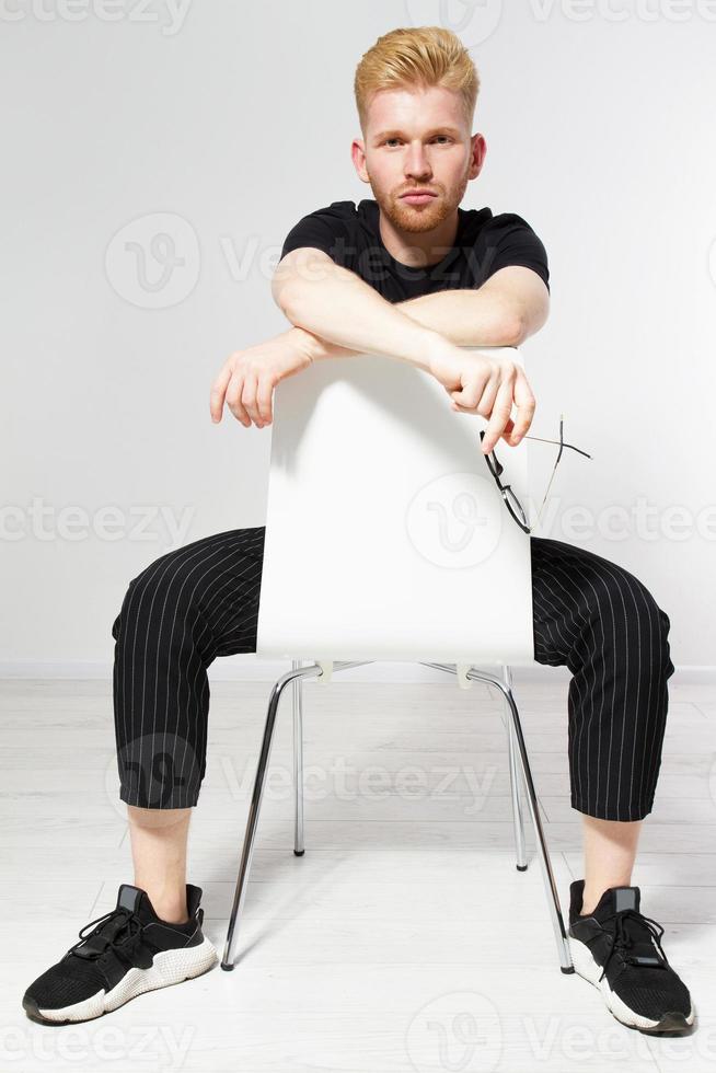 jeune homme sur une chaise, portrait d'un beau jeune homme assis sur une chaise, fier et satisfait jeune homme assis sur une chaise et regardant la caméra isolée, jeune homme décontracté à lunettes photo