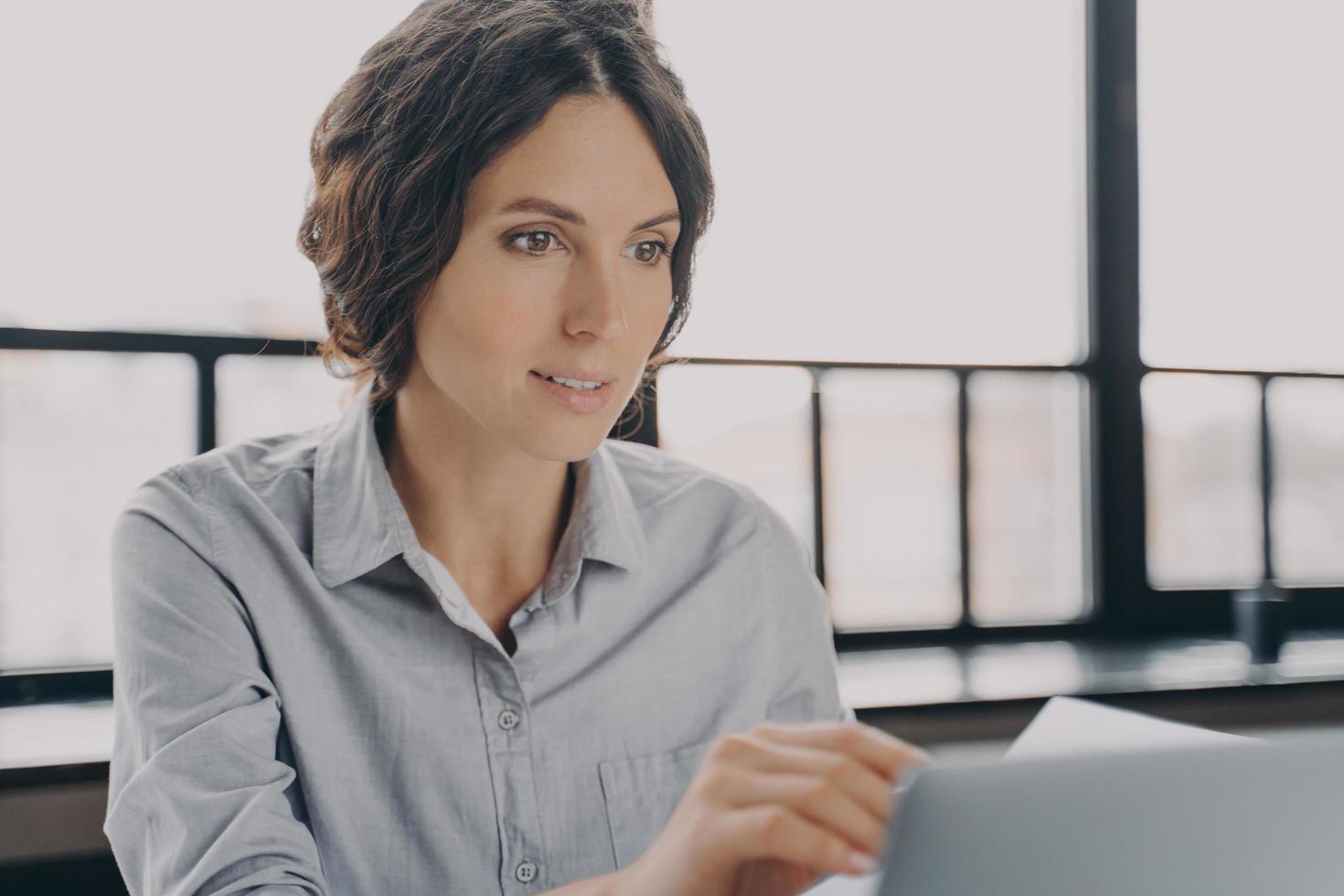 jeune employée de bureau assise sur le lieu de travail et travaillant en ligne sur un ordinateur portable, photo