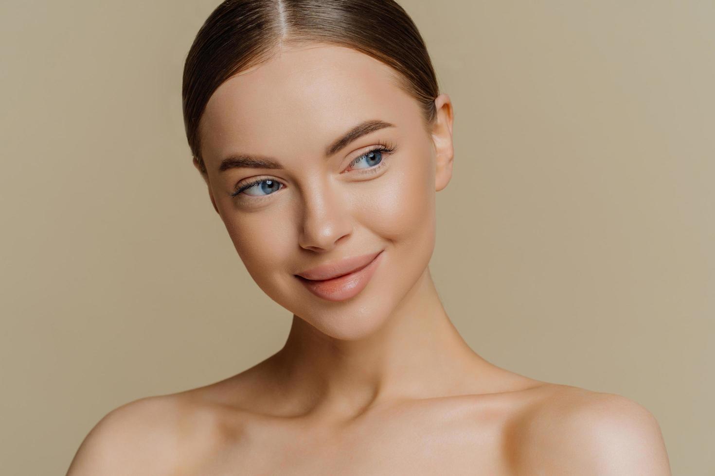 portrait d'une femme à moitié nue rêveuse réfléchie regarde de côté avec une expression satisfaite applique un maquillage minimal a une peau fraîche et propre après les procédures de beauté du visage isolées sur fond beige photo