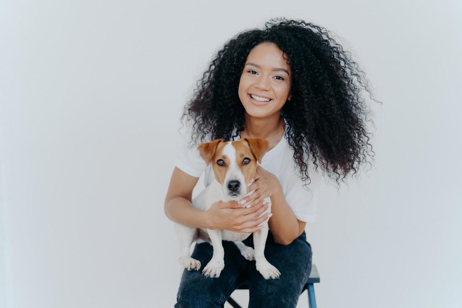 photo d'une femme heureuse à la peau sombre étant pour toujours avec un chiot de race, aime les loisirs à la maison, est assise sur une chaise, isolée sur fond blanc. lien humain et animal. confiance et amitié