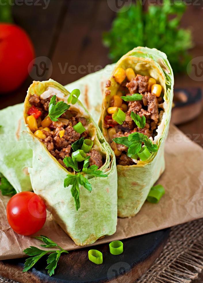 Burritos s'enroule avec du boeuf haché et des légumes sur un fond en bois photo