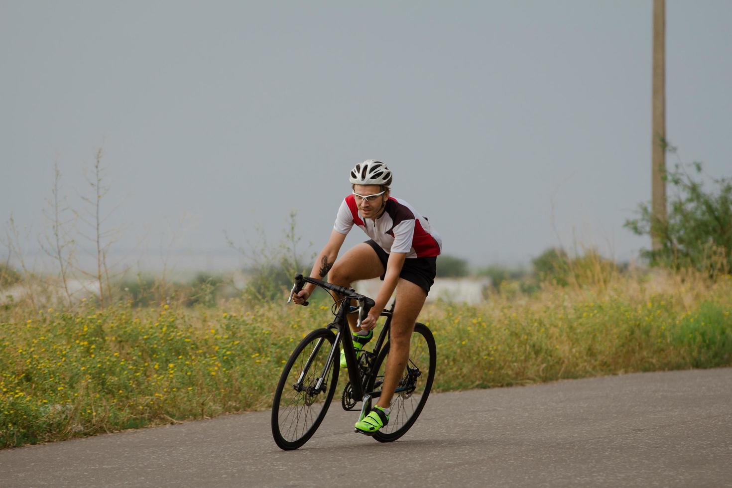 coureur cycliste en casque et vêtements de sport s'entraînant seul sur une route de campagne vide, des champs et des arbres sur fond photo