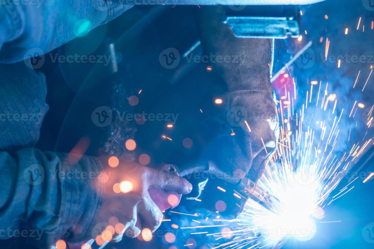 soudeur soudant le métal avec une machine de soudage à l'arc sous argon et a des étincelles de soudage. un homme porte un masque de soudage et des gants de protection. sécurité sur le lieu de travail industriel. soudeur travaillant en toute sécurité. industrie sidérurgique. photo