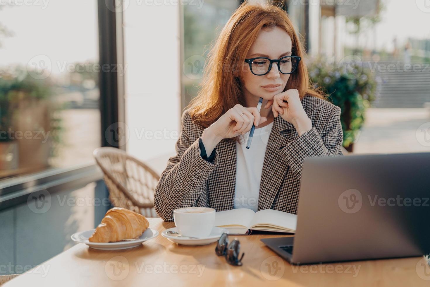 une femme d'affaires sérieuse au gingembre en tenue de soirée travaille à la cafétéria développe un nouveau projet de démarrage photo