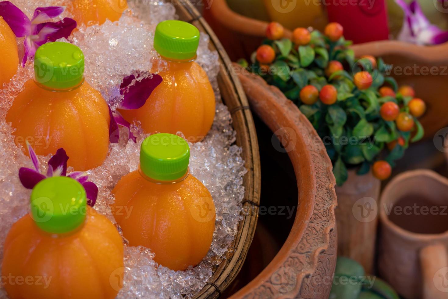 bouteille de jus d'orange dans la glace avec des fleurs de pois papillon. photo