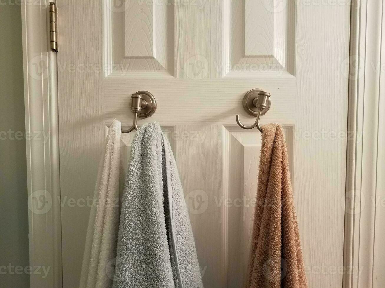 serviettes suspendues à des crochets sur la porte de la salle de bain blanche photo