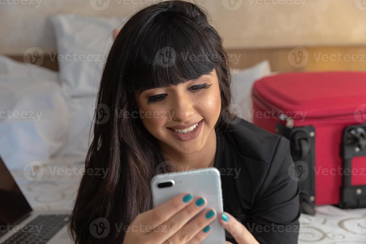 jolie jeune femme avec valise dans un appartement d'hôtel moderne à l'aide de téléphone. disant à sa famille qu'elle est bien arrivée à destination et qu'elle est déjà à l'hôtel. photo