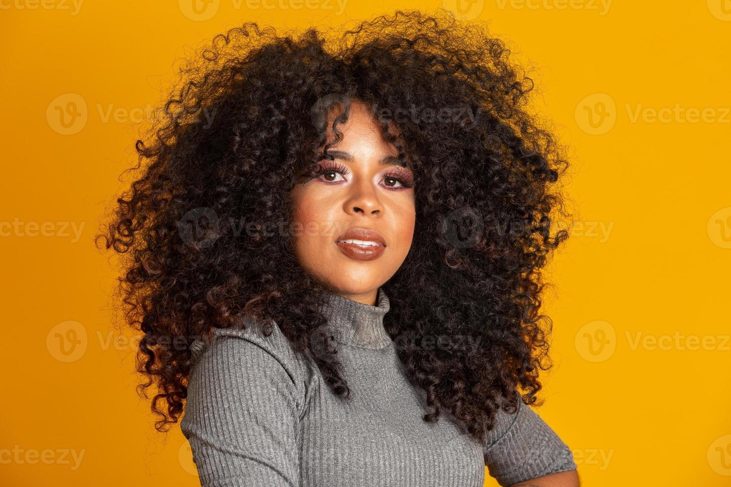 portrait de beauté d'une femme afro-américaine avec une coiffure afro et un maquillage glamour. femme brésilienne. race mixte. cheveux bouclés. coiffure. fond jaune. photo