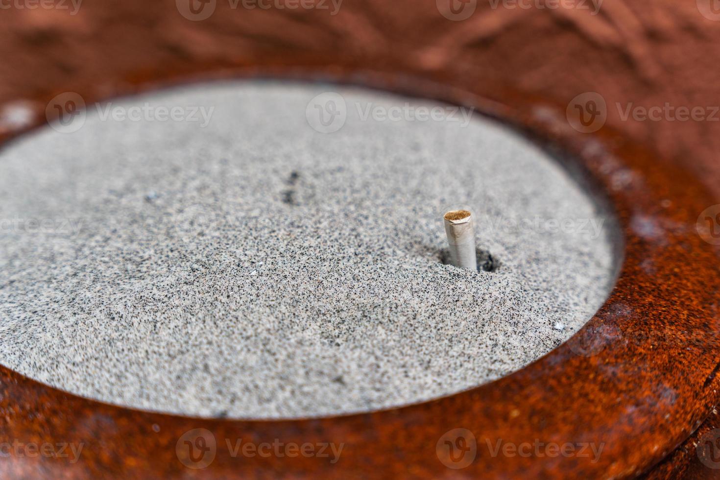 Filtre de cigarette usagé en tas de sable sur cendrier photo