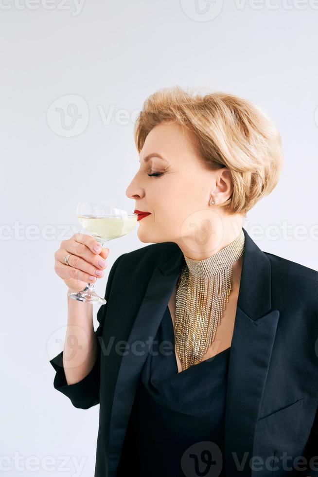 femme élégante et élégante mature en smoking avec un verre de vin mousseux. fête, célébration, concept anti-âge photo