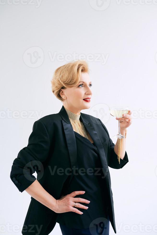 femme élégante et élégante mature en smoking avec un verre de vin mousseux. fête, célébration, concept anti-âge photo