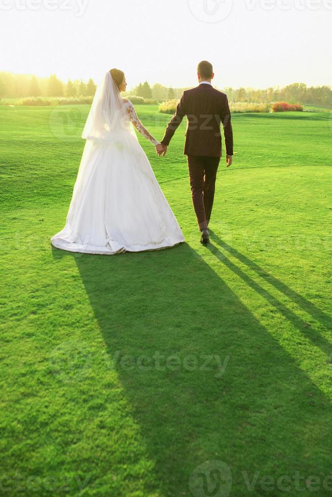 couple de mariage en robe de mariée et costume en regardant le coucher du soleil sur le terrain. amour, famille, concept de tendresse photo