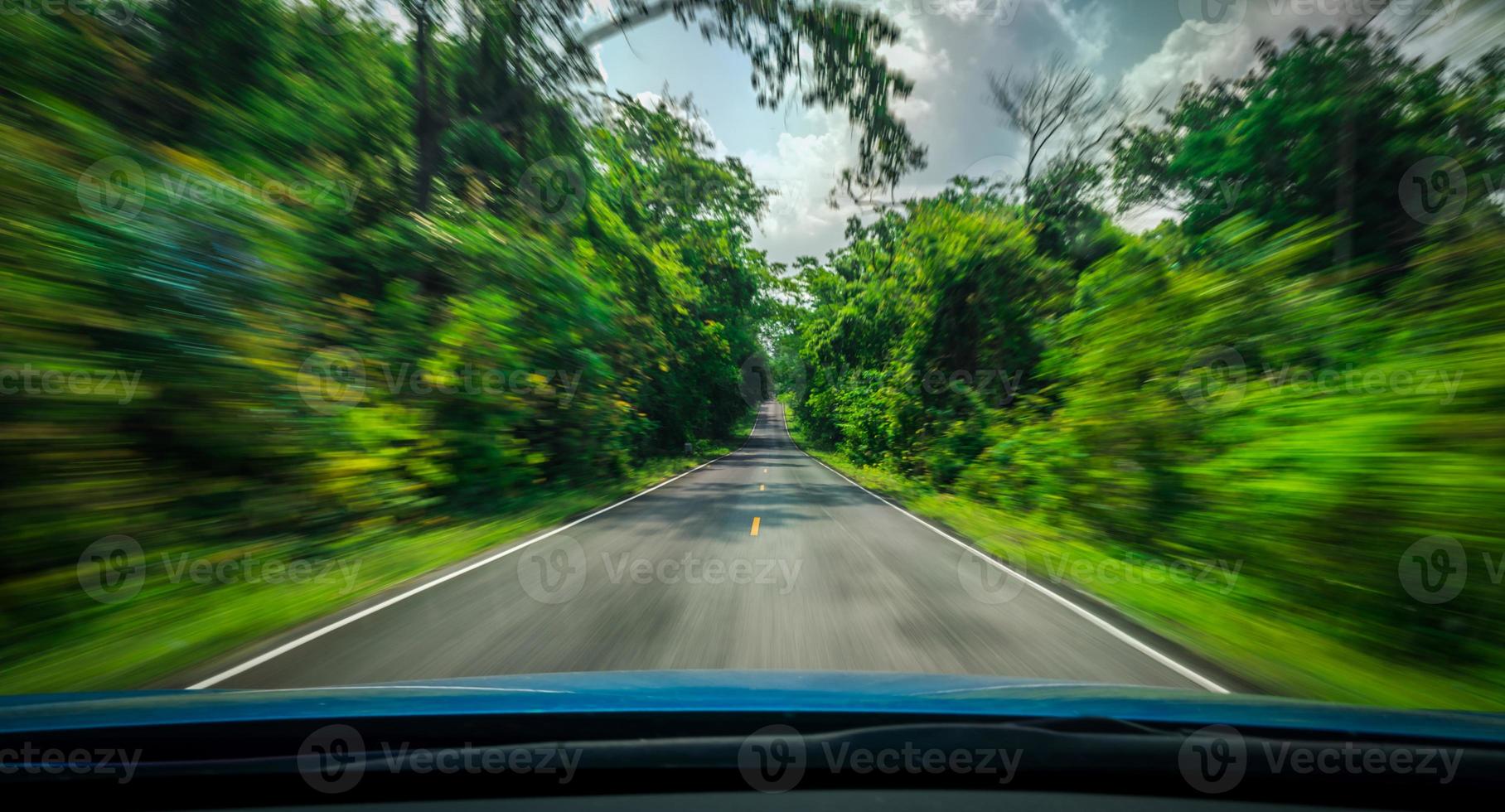 Vue de l'avant de la voiture bleue sur route goudronnée et flou de mouvement de vitesse sur l'autoroute en été avec forêt d'arbres verts à la campagne photo