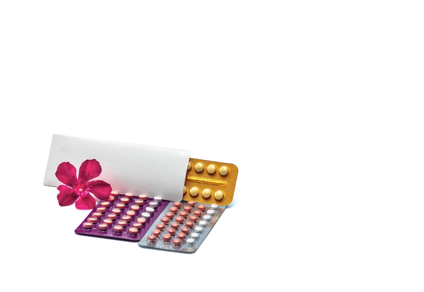 pilules contraceptives ou pilules contraceptives avec fleur rose sur fond blanc avec espace de copie. hormone pour la contraception. concept de planification familiale. comprimés ronds d'hormones sous blister. photo