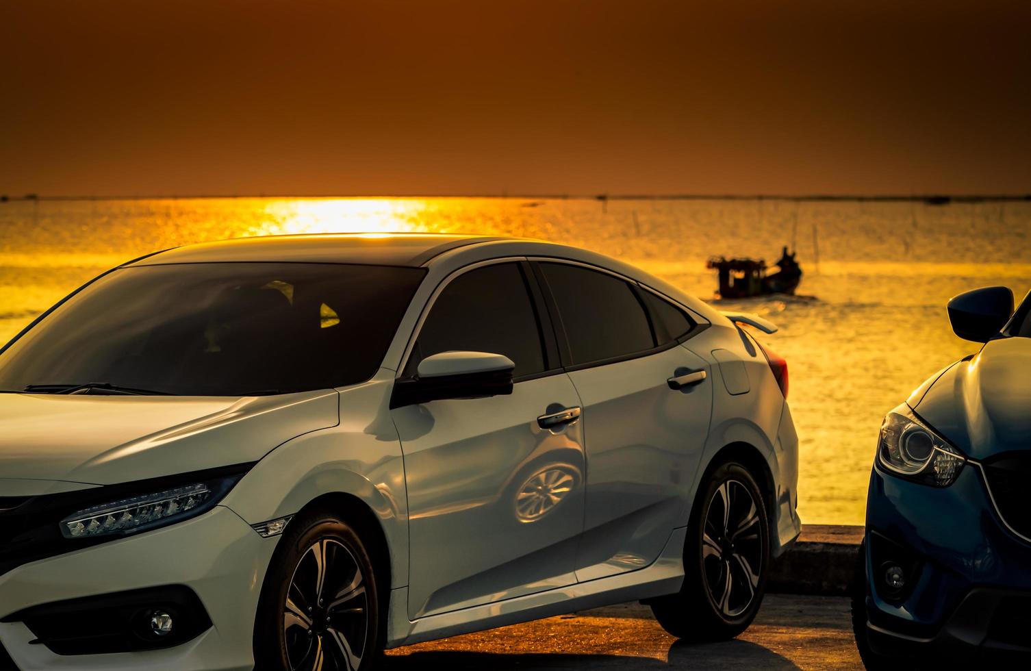 vue de face d'une voiture compacte blanche et bleue garée sur une route en béton au bord de la plage au coucher du soleil. technologie des voitures électriques et hybrides. concept d'entreprise de l'industrie automobile. voyage sur la route pendant les vacances d'été. photo