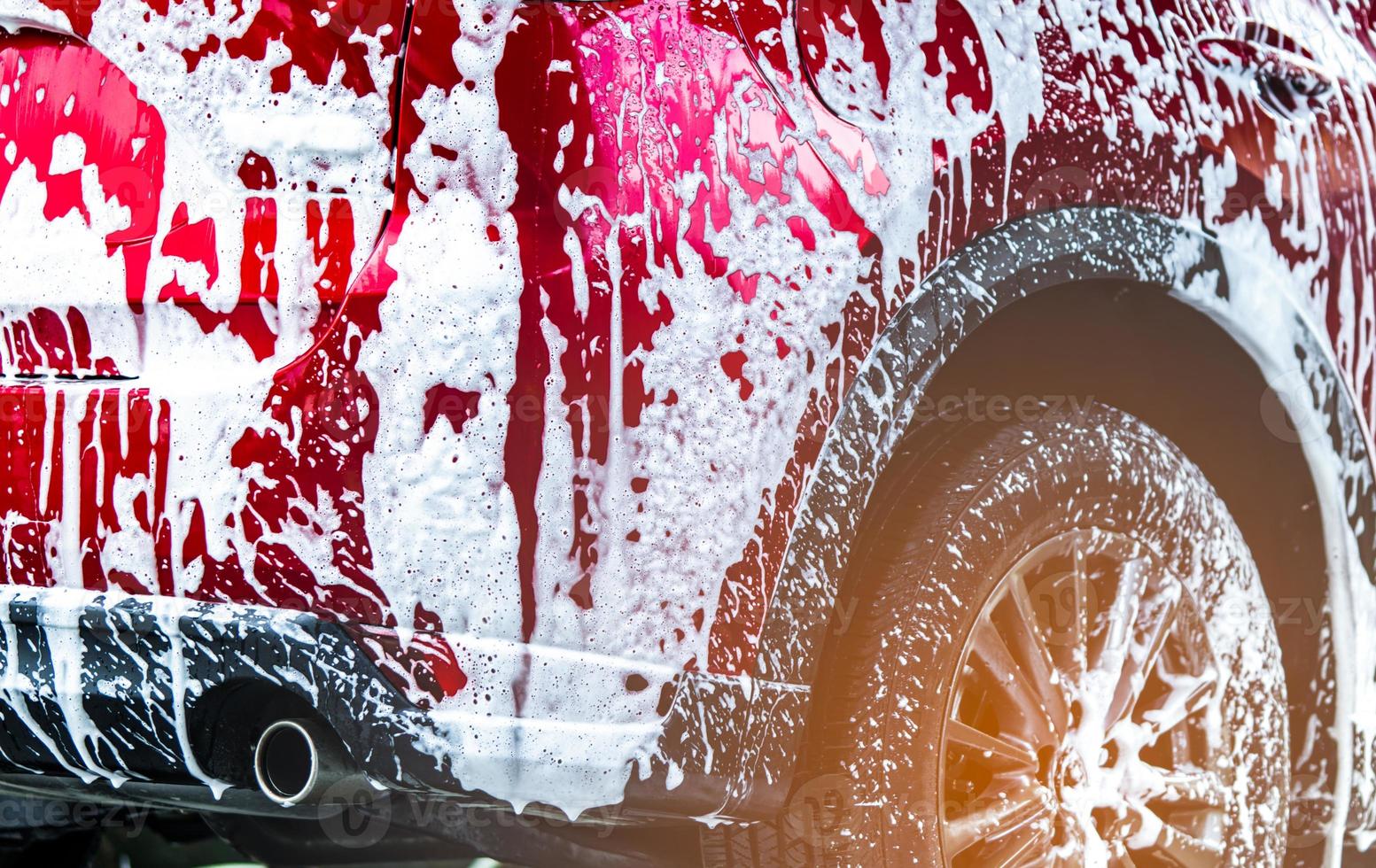 voiture suv compacte rouge avec un design sportif et moderne à laver avec du savon. voiture recouverte de mousse blanche. concept d'entreprise de service d'entretien automobile. lavage de voiture avec de la mousse avant le cirage du verre et le revêtement du verre automobile. photo