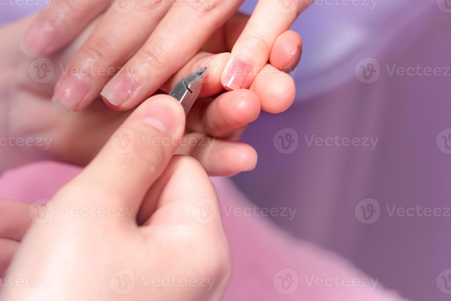 femme recevant un service de manucure des ongles par une manucure professionnelle au salon de manucure. l'esthéticienne utilise une tondeuse pour nettoyer et couper la cuticule au salon de manucure et de spa. thérapie des mains et des ongles par un thérapeute. photo