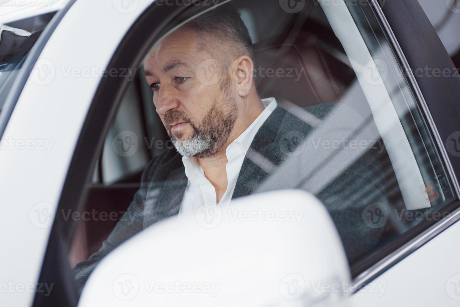 photo du conducteur dans le véhicule. homme d'affaires senior sérieux testant une nouvelle voiture